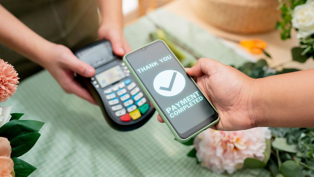 Urban Ledger POS terminal with staff member collecting a QR payment in a retail setting, highlighting mobile tap-to-pay
